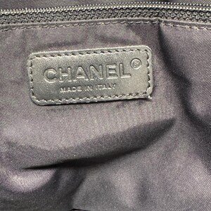K&ouml;nnte beinhalten: Nahaufnahme eines schwarzen Lederetiketts mit dem gepr&auml;gten Wort "CHANEL" und dem Text "MADE IN ITALY". Das Etikett ist auf einem schwarzen Stoff befestigt, m&ouml;glicherweise die Innenseite einer Tasche. Oben ist ein schwarzer Rei&szlig;verschluss zu sehen.