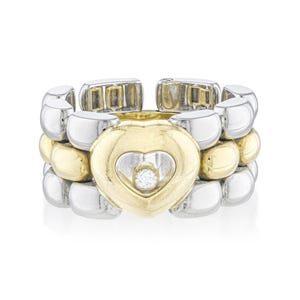 May include: A two-tone ring featuring a gold heart-shaped center with a small diamond and a silver and gold band. The ring has a unique design with a heart-shaped centerpiece and a flexible band.