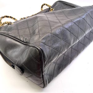 May include: Black quilted leather handbag with gold-tone chain straps. The bag features a diamond pattern and a zipper closure. The bag is a classic style, suitable for everyday use.