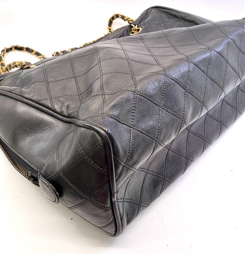 May include: Black quilted leather handbag with gold-tone chain straps. The bag features a diamond pattern and a zipper closure. The bag is a classic style, suitable for everyday use.