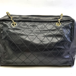 May include: Black quilted leather handbag with gold-tone chain straps. The bag features a diamond pattern and a top zipper closure. The bag has a rectangular shape and is likely a shoulder bag or tote.