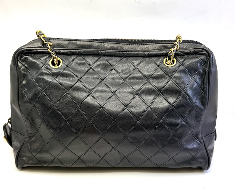 May include: Black quilted leather handbag with gold-tone chain straps. The bag features a diamond pattern and a top zipper closure. The bag has a rectangular shape and is likely a shoulder bag or tote.