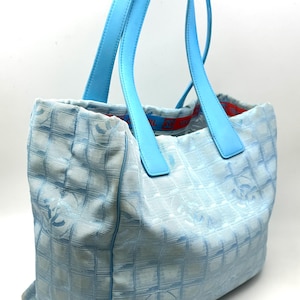 Puede incluir: Bolso tote azul claro con asas azul cielo a juego. El bolso presenta un patr&oacute;n acolchado con un dise&ntilde;o de logotipo repetido. El forro interior es rojo con una banda con el logotipo. Un accesorio elegante y funcional.