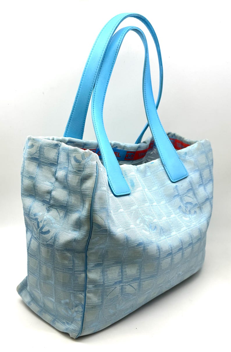 Puede incluir: Bolso tote azul claro con asas azul cielo a juego. El bolso presenta un patr&oacute;n acolchado con un dise&ntilde;o de logotipo repetido. El forro interior es rojo con una banda con el logotipo. Un accesorio elegante y funcional.