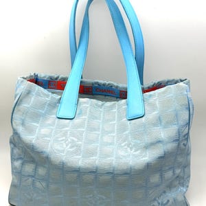 Puede incluir: Bolso tote de color azul claro con asas a juego. El bolso presenta un patr&oacute;n repetido de Cs entrelazadas y una banda azul y roja con el nombre de la marca. Las asas son de un tono azul m&aacute;s claro.