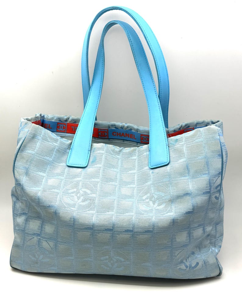 Puede incluir: Bolso tote de color azul claro con asas a juego. El bolso presenta un patr&oacute;n repetido de Cs entrelazadas y una banda azul y roja con el nombre de la marca. Las asas son de un tono azul m&aacute;s claro.