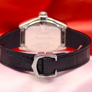 May include: A silver wristwatch with a black leather band. The watch face is rectangular and has a silver frame. The band has a silver buckle with the letter 'C' on it.