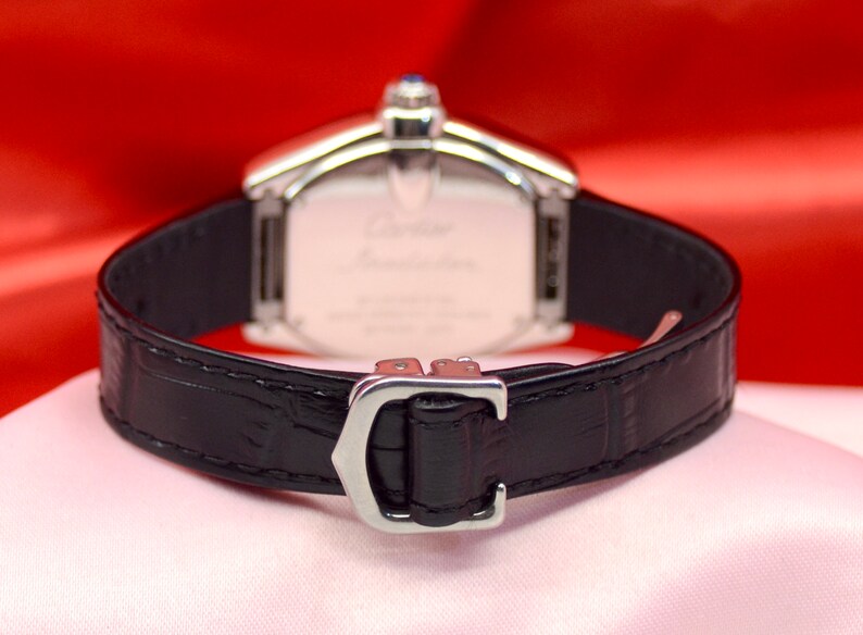 May include: A silver wristwatch with a black leather band. The watch face is rectangular and has a silver frame. The band has a silver buckle with the letter 'C' on it.