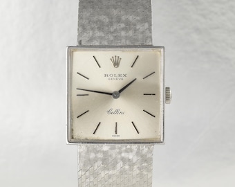 May include: A silver-toned Rolex Cellini wristwatch featuring a square case and a textured, woven-style metal bracelet. The dial is light-colored with thin black hour markers, black hands, and the text Rolex Geneve Cellini Swiss printed on it.