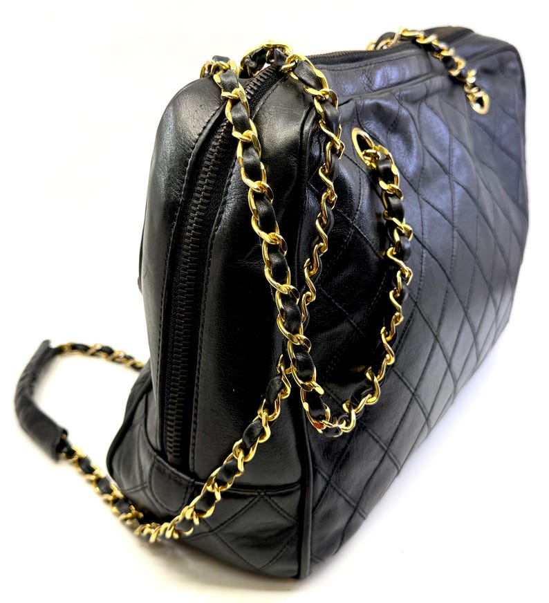 May include: Black quilted leather handbag with gold-tone chain straps. The bag features a diamond pattern and a top zipper closure. The chain strap is interwoven with black leather. A classic and elegant accessory.
