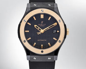 Op de afbeelding: Een automatisch polshorloge van Hublot Geneve met een zwarte, getextureerde wijzerplaat en goudkleurige wijzers en uurmarkeringen. Het horloge heeft een ronde gouden lunette vastgezet met zes schroeven, een zwarte rubberen band en een datumvenster met het getal 27.