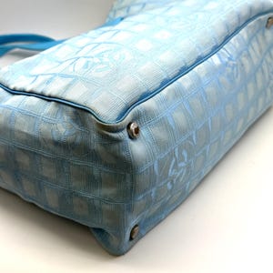 Puede incluir: Bolso de mano azul claro con un patr&oacute;n de cuadr&iacute;cula y un asa azul a juego. El bolso presenta herrajes plateados en las esquinas y un dise&ntilde;o de logotipo sutil. El bolso est&aacute; hecho de una tela texturizada.