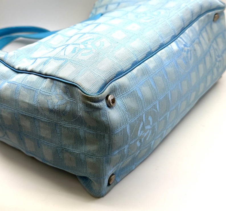 Puede incluir: Bolso de mano azul claro con un patr&oacute;n de cuadr&iacute;cula y un asa azul a juego. El bolso presenta herrajes plateados en las esquinas y un dise&ntilde;o de logotipo sutil. El bolso est&aacute; hecho de una tela texturizada.