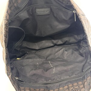 K&ouml;nnte beinhalten: Offene Ansicht einer braunen und schwarzen Tragetasche mit sich wiederholendem Muster. Die Tasche hat schwarze Griffe und ein schwarzes Innenfutter mit mehreren F&auml;chern. Ein kleines Lederetikett mit dem Markennamen ist innen sichtbar.