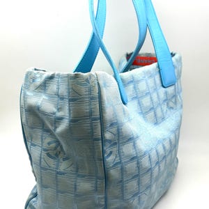 Puede incluir: Bolso tote azul claro con asas a juego. El bolso presenta un patr&oacute;n de cuadr&iacute;cula con logotipos repetidos. Las asas son de un tono azul m&aacute;s claro. El bolso est&aacute; hecho de un material suave.