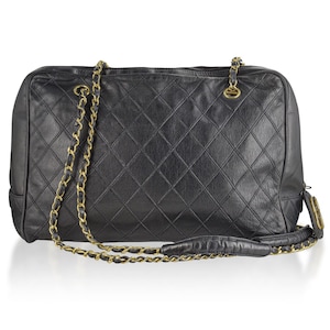 May include: Black quilted leather handbag with gold-tone chain straps. The bag features a diamond pattern and a top zipper closure. The shoulder strap is a combination of leather and chain. The bag has a rectangular shape.