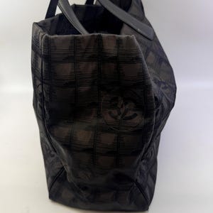 May include: Black tote bag with a checkered pattern. The bag has two black handles and a logo on the side. The bag is made of a fabric material.
