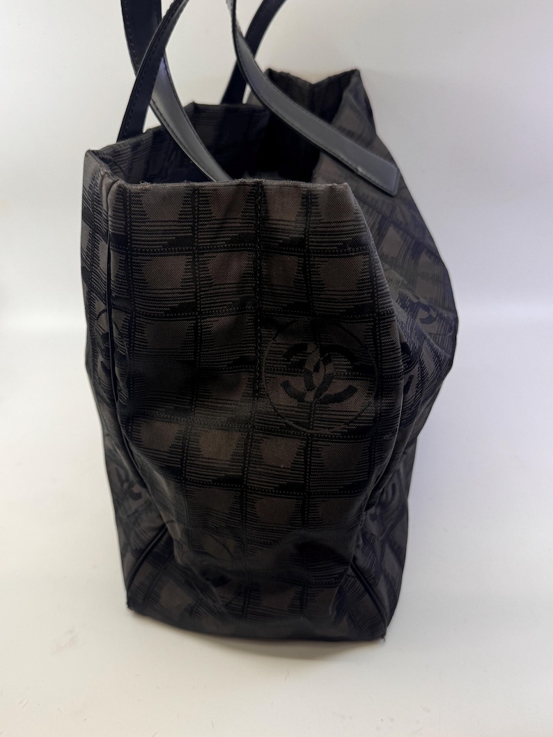 May include: Black tote bag with a checkered pattern. The bag has two black handles and a logo on the side. The bag is made of a fabric material.
