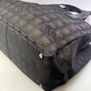 May include: A black tote bag with a repeating pattern of interlocking Cs. The bag has a rectangular shape with a flat bottom and a top handle. The bag's corners have silver-colored metal studs.