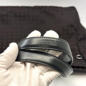 K&ouml;nnte beinhalten: Nahaufnahme eines schwarzen Lederhandtaschengriffs. Der Griff ist dick und gen&auml;ht, mit einer glatten, gl&auml;nzenden Oberfl&auml;che. Der Hintergrund ist ein dunkelbrauner Stoff mit einem dezenten Muster. Die Tasche scheint eine Tragetasche oder eine Umh&auml;ngetasche zu sein.