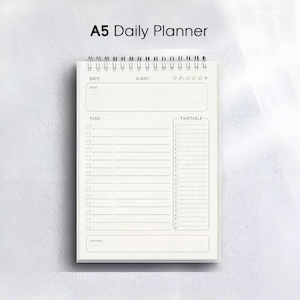 Op de afbeelding: A5 Daily Planner met een witte kaft en spiraalbinding. De planner bevat secties voor datum, D-day, taken en een tijdschema. De tekst "A5 Daily Planner" staat bovenaan afgedrukt.