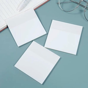 May include: Three white square sticky notes with a lighter top section are arranged on a light blue surface. A notebook and pen are visible in the background, along with a pair of glasses.