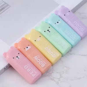 Könnte beinhalten: Sechs bunte Textmarker in Bärenform in Pastelltönen von Rosa, Orange, Gelb, Grün, Blau und Lila. Jeder Textmarker hat ein anderes Bärengesicht und die Aufschrift "PERO" oder "BOOW" auf dem Körper.