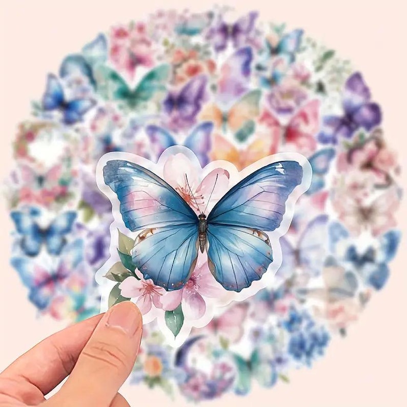 May include: A collection of butterfly stickers in various colors, including blue, pink, and purple. The stickers feature watercolor designs of butterflies and flowers. A hand holds a sticker with a large blue butterfly.