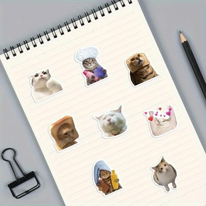 Op de afbeelding: Een verzameling van negen stickers met katten als thema op een gelijnd notitieblok. De stickers bevatten verschillende kattenillustraties, waaronder katten met hoeden, in handdoeken gewikkeld en omringd door harten. De stickers zijn in verschillende kleuren en poses.