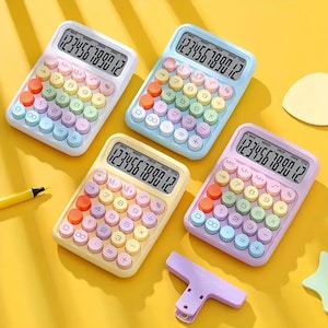 Könnte beinhalten: Vier pastellfarbene Taschenrechner mit regenbogenfarbenen Tasten und Digitalanzeigen. Die Rechner sind auf einer gelben Oberfläche angeordnet. Ein lila Clip und ein gelber Stift sind ebenfalls sichtbar.