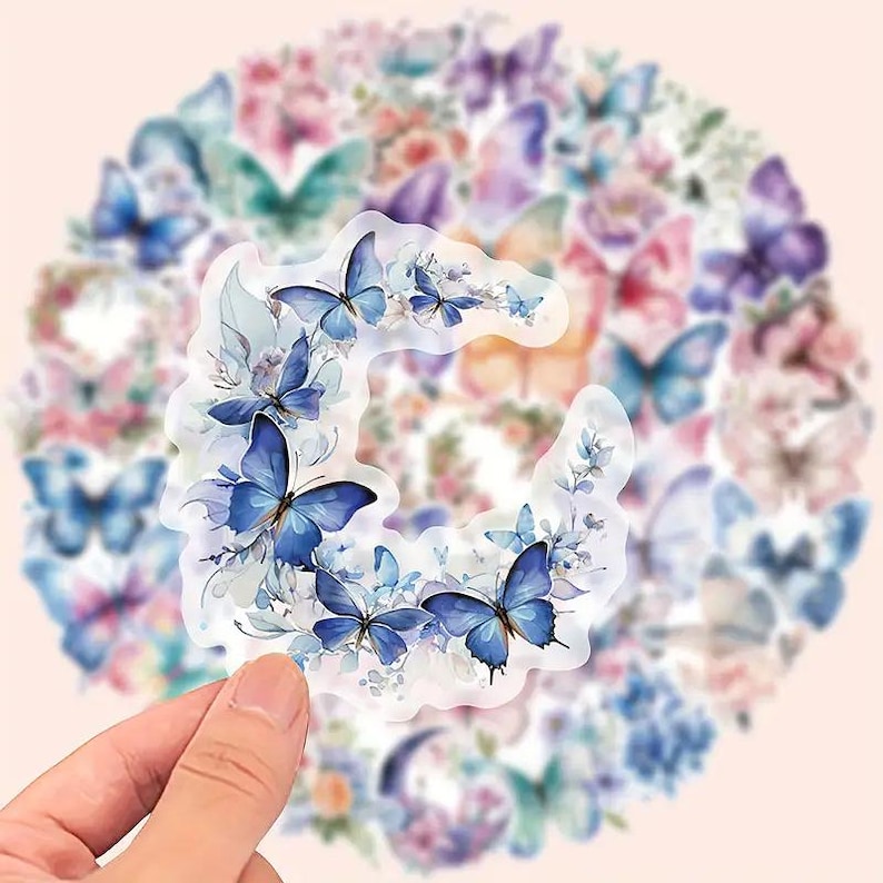 May include: A collection of butterfly stickers in various shades of blue, purple, and pink. The stickers feature detailed butterfly designs with floral accents. The background is a soft pink, creating a delicate and artistic aesthetic.