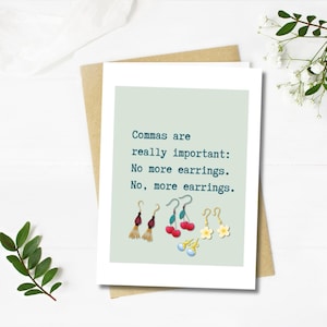 May include: A white greeting card with the text "Commas are really important: No more earrings. No, more earrings." The card shows illustrations of different earrings, such as tassel, cherry, and flower designs.