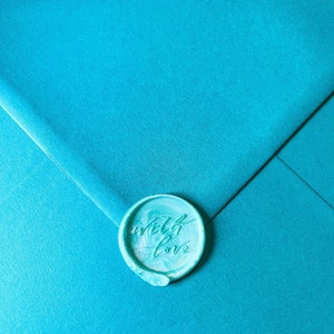 May include: A teal envelope sealed with a matching wax stamp. The stamp is round and features the words "with love" in cursive script. The envelope has a textured surface.
