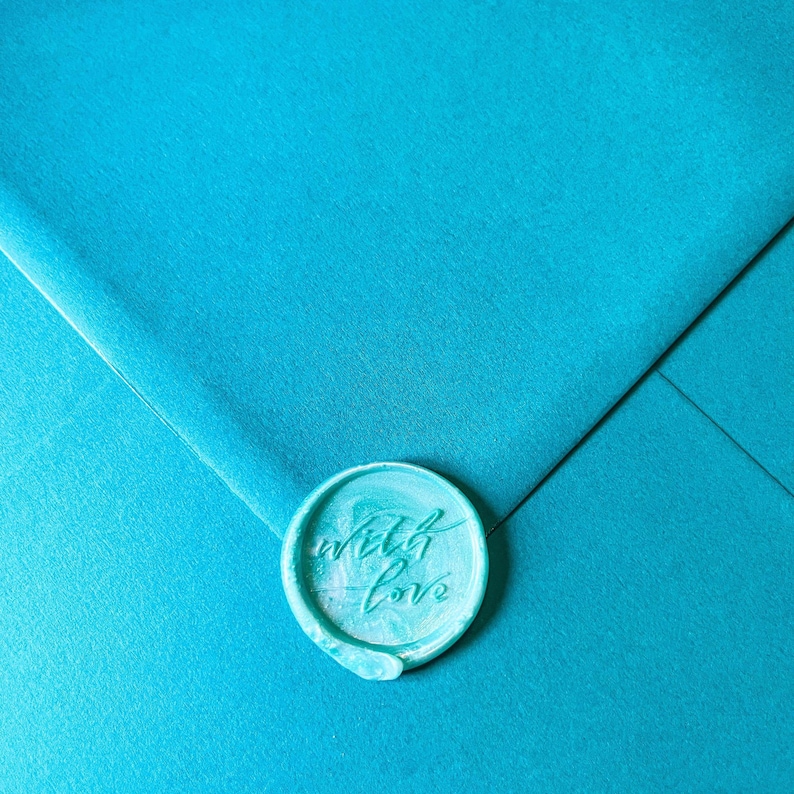 May include: A teal envelope sealed with a matching wax stamp. The stamp is round and features the words "with love" in cursive script. The envelope has a textured surface.