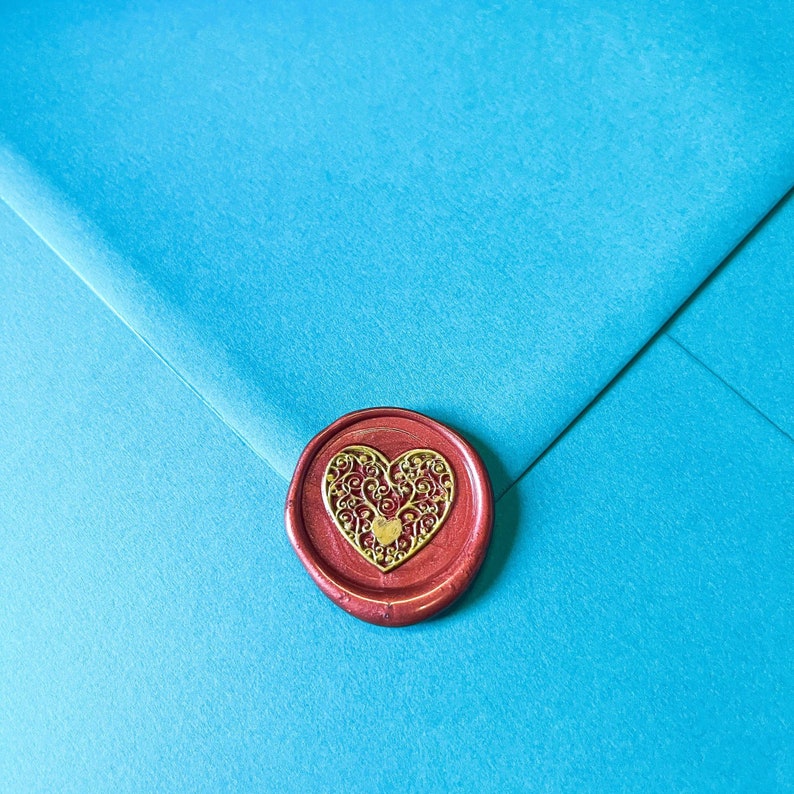 May include: A close-up of a teal envelope sealed with a red wax stamp. The stamp features a gold filigree heart design. The envelope's texture is visible, and the overall composition is clean and elegant.