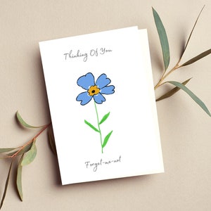 May include: A white card with the text "Thinking of You" and a blue forget-me-not flower with a yellow centre. The text "Forget-me-not" is written below the flower.