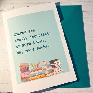 May include: A white greeting card with a light blue rectangular centre featuring the text: Commas are really important: No more books. No, more books. Below the text are two stacks of colourful illustrated books and a small pink mug.