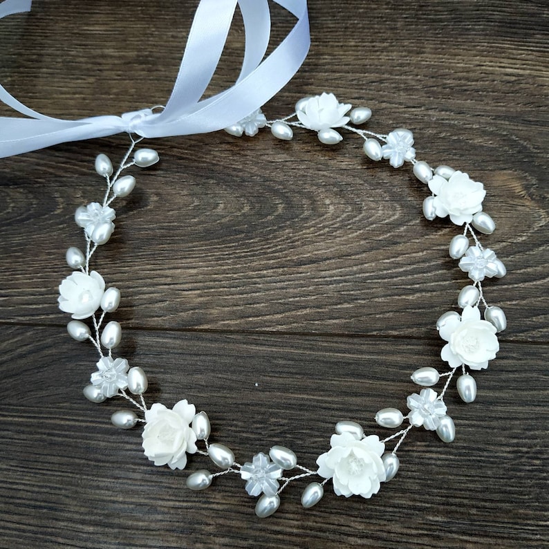 May include: A white floral crown with pearl accents. The crown is made of white flowers and pearls on a silver wire base.