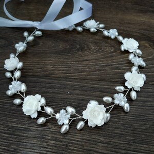 May include: A white floral headband with pearl accents. The headband is made of wire and has a ribbon attached.