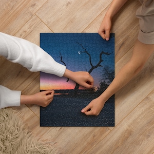 May include: Two people are putting together a jigsaw puzzle of a landscape with a crescent moon in the sky. The puzzle shows a lake with a sunset and two bare trees.
