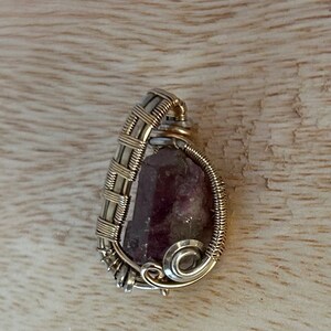May include: A purple and green gemstone wrapped in gold and silver wire, creating a pendant.
