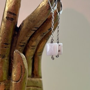 May include: A pair of silver dangle earrings with a white and gray square-shaped stone pendant.