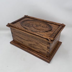 May include: A wooden box with a carved design on the lid. The box is made of dark wood and has a rectangular shape.