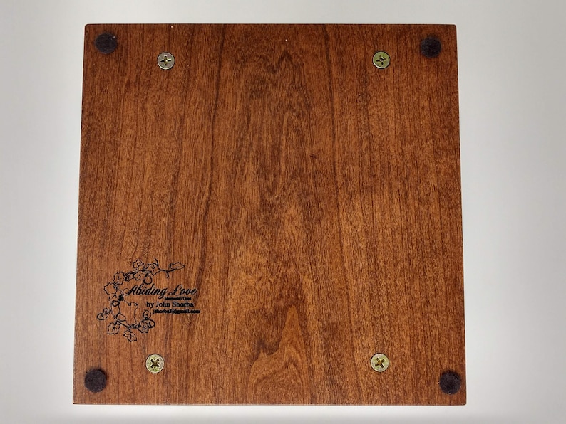 May include: A wooden box with a dark brown stain. The box has a black felt bottom and four black felt feet. The box has a black inscription that reads "Abiding Love by John Sharpe".