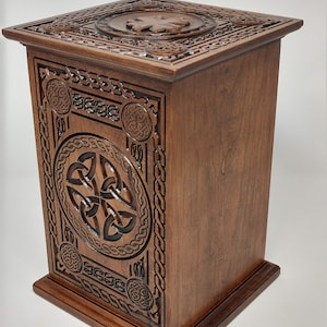 May include: A wooden box with intricate Celtic knot carvings. The box is made of dark brown wood and has a square shape. The top of the box is decorated with a Celtic knot design.