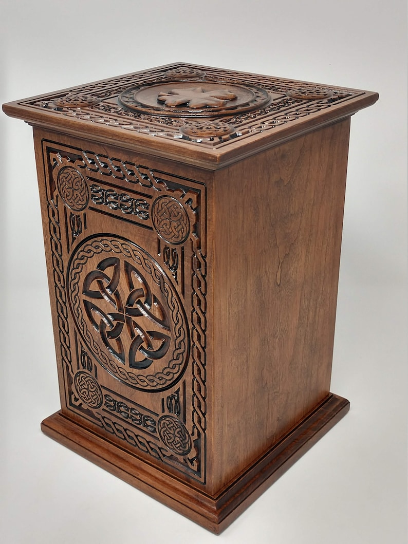 May include: A wooden box with intricate Celtic knot carvings. The box is made of dark brown wood and has a square shape. The top of the box is decorated with a Celtic knot design.
