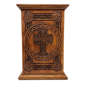 May include: A wooden box with a Celtic cross design carved into the front. The box is brown and has a decorative trim around the edges.