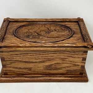 May include: A wooden box with a carved design of a bird on the lid. The box is made of dark brown wood and has a simple, elegant design.