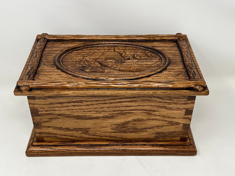 May include: A wooden box with a carved design of a bird on the lid. The box is made of dark brown wood and has a simple, elegant design.