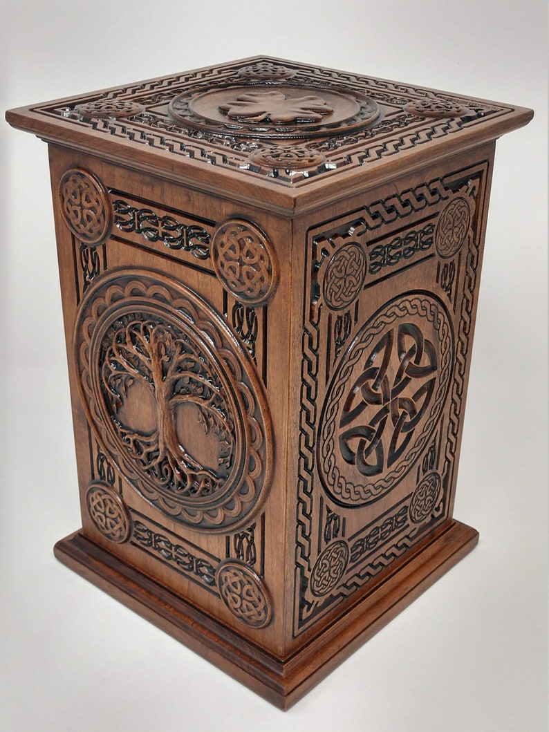May include: A wooden box with intricate Celtic knotwork carvings. The box features a tree of life design on one side and a shamrock on the top.